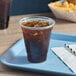 A plastic cup with a brown drink and ice on a tray with a straw
