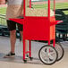 A man standing next to a red Carnival King popcorn cart full of popcorn.