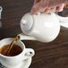 A hand pouring tea from a Homer Laughlin Seville beverage server into a white mug.