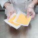 A person's hand in a plastic glove using Choice patty paper to hold cheese.