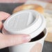 A person holding a coffee cup with a Solo white plastic dome lid on it.