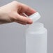 A hand holding a white plastic squeeze bottle with a thin dispensing valve.