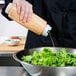 A person using a FIFO Innovations squeeze bottle to pour dressing onto a bowl of lettuce.