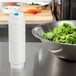 A white bottle of FIFO Innovations Squeeze Bottle with Thin Dispensing Valve next to a bowl of salad.