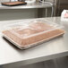 A brown chocolate cake in a Solut plastic container with a clear lid on a table.