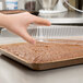 A hand holding a clear plastic container over a brownie in a Solut kraft sheet pan.
