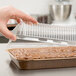 A hand holding a Solut clear plastic container over a brownie in a brown Solut sheet pan.