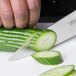 A person using a Mercer Culinary Genesis Forged Chef Knife to cut a cucumber.