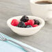 An Acopa ivory stoneware fruit bowl filled with berries on a napkin next to a cup of coffee.