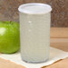 A translucent plastic lid on a glass of water next to a green apple.