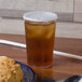 A glass of iced tea with a straw and a black lid on a table with a plate of food.