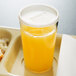 A translucent plastic lid on a white tray with a glass of orange juice and food.