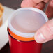 A person using a Dinex translucent disposable lid on a plastic cup.