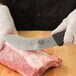 A gloved hand uses a Victorinox beef skinning knife to cut meat.