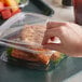 A close up of a hand holding a Dart Deli container with food in it.