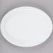 A Tuxton bright white narrow rim oval china platter on a gray surface.