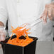 A person using Visions clear plastic tongs to serve shredded carrots into a container.