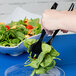 A person holding a black Visions plastic serving fork over a salad.