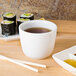 A CAC Super White Chinese tea cup filled with tea on a table with sushi.