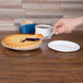 A hand holding a Visions clear plastic pie server over a slice of pie on a plate.
