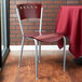 A Lancaster Table & Seating mahogany finish cafe chair with a red table cloth on it sitting in front of a table.