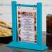 A Menu Solutions sky blue wood flip top table tent on a table with a sandwich and chips.