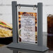 A Menu Solutions ash wood table tent on a table with a menu showing a sandwich.