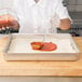 A person wearing a white shirt and gloves uses an American Metalcraft aluminum pan to mix red sauce.