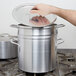 A hand opening the lid on a large Vollrath silver double boiler.