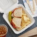 A sandwich in a EcoChoice Bagasse take-out box with chips and a drink.