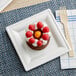A small chocolate cake with raspberries and whipped cream on an EcoChoice Bagasse square plate.
