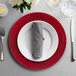 A table set with a red 10 Strawberry Street lacquer charger, silverware, and a glass of water.