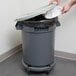 A person using a hand to put a Continental Huskee plastic lid on a gray trash can.