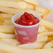 A Solo translucent polystyrene souffle cup of ketchup on french fries.