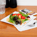 A white WNA Comet Milan plastic salad plate with salad on it on a table.