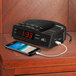 A black Conair alarm clock radio with a cell phone charging on it.