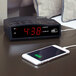 A black Conair digital alarm clock with a cell phone charging on it.