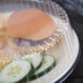 A Dart clear plastic dome plate cover over a plastic container with a hamburger and cucumber sandwich inside.