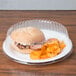 A Dart clear plastic dome plate cover over a plate with a sandwich and potato chips.