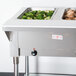 A stainless steel Advance Tabco electric hot food table with two pans of food on a counter.