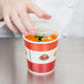 A hand reaching for a Choice paper soup and food container filled with food.