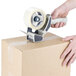 A hand using a Lavex Packaging tape dispenser to seal a box.