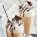 Two glasses of milkshakes topped with HERSHEY'S Special Dark Chocolate Syrup and whipped cream.
