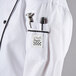 A close up of a white Chef Revival ladies long sleeve coat with black piping and a pocket with a pen in it.