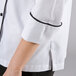 A woman's white Chef Revival long sleeve coat with black piping on the arm.