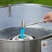 A hand using a Carnival King Floss Bowl Stabilizer Net to pour blue liquid into a metal container.