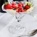 A Libbey Deliss sundae dish filled with fruit and berries on a table with a spoon.