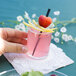 A hand holding a Libbey votive shot glass of pink liquid with a strawberry on top.
