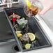 A hand pouring a drink into a black Bar Maid drain tray with ice and lemons.