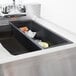 A Bar Maid black plastic drain tray in a sink with a black container filled with ice and lemons.